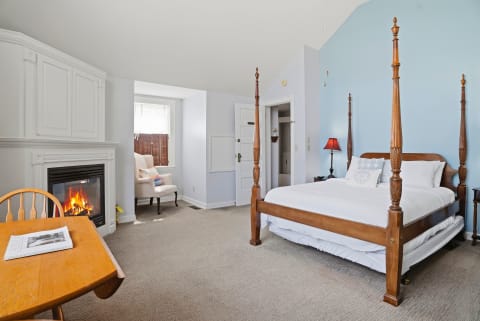 A calm bedroom with a wooden four-poster bed, an armchair, and a fireplace.