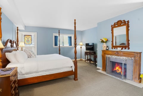 A cozy bedroom featuring a four-poster bed, bright blue walls, and an ornate fireplace.