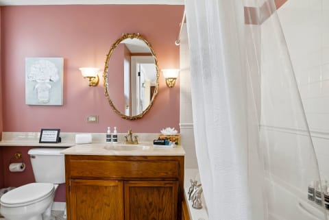 A serene private bathroom featuring pink walls, a golden mirror, and marble finishes.