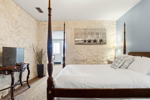 Elegant bedroom with a four-poster bed, stone walls, and a television on a wooden console.