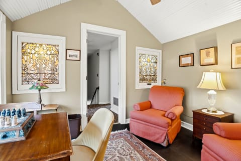 A comfortable sitting room featuring coral armchairs, stained glass windows, a wooden desk with a chess set, and decorative wall art.