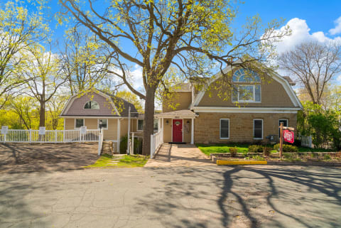 Stone farmhouse with modern features, red entrance, and mature trees.