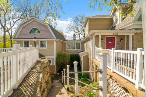 A vacation home entrance with a red door, wood siding, and stone steps surrounded by greenery.