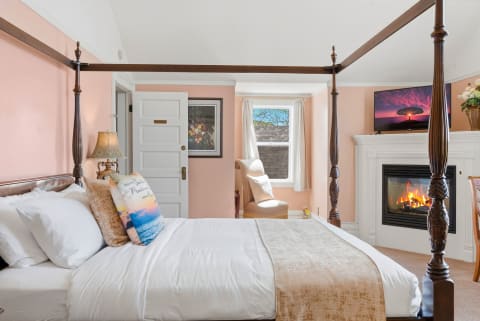A serene bedroom featuring a four-poster bed, TV, and fireplace.