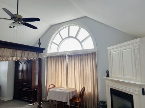 A spacious room with a vaulted ceiling, large circular window, beige curtains, and classic wooden furniture.