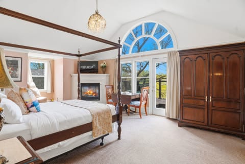 Luxurious bedroom featuring a four-poster bed, fireplace, and large arched window with scenic views.
