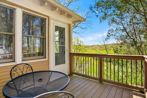 A black table and chair on a balcony with a view of green hills and trees.