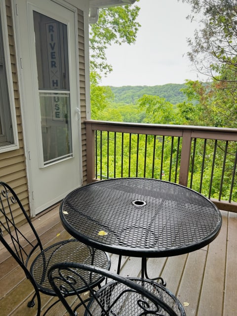 Black wrought-iron table and chairs on a balcony overlooking green hills and trees.