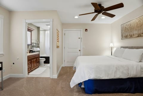 A peaceful bedroom with a plush bed, ceiling fan, and visible ensuite bathroom.