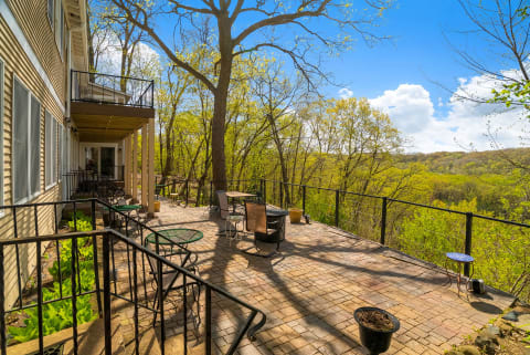 A large patio with various seating arrangements overlooking a green valley and bright blue sky.