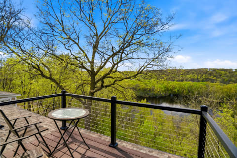 A private deck with chairs overlooking a scenic view of green trees and a peaceful lake under a clear blue sky.