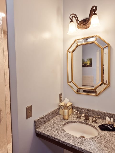 A stylish bathroom featuring a granite countertop, gold fixtures, and a decorative mirror.