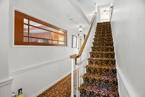 Charming staircase with a floral runner and classic wood railings leading to upstairs areas, featuring warm lighting.
