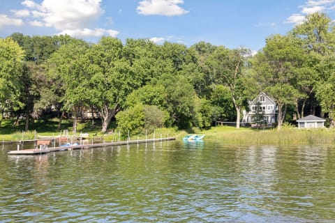 A view of a lakeside house surrounded by trees and a dock with kayaks.