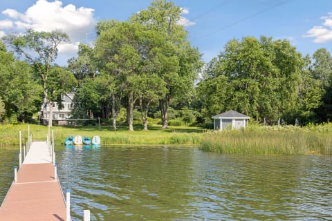 Lakeside view with a wooden dock, paddle boats, and greenery in the background.