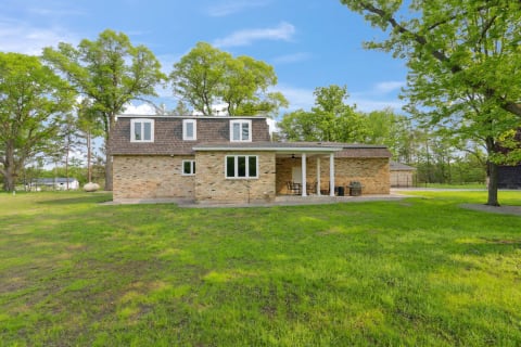 A brick house with a shingled roof sitting on a green lawn under a clear blue sky.