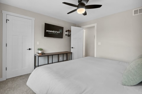 Contemporary bedroom with a white bed, green pillows, and a flat-screen TV.