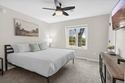 Modern bedroom with a queen-sized bed, a window view of greenery, and a wall-mounted TV.