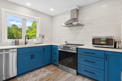 A contemporary kitchen with blue cabinets, stainless steel appliances, and a large window.