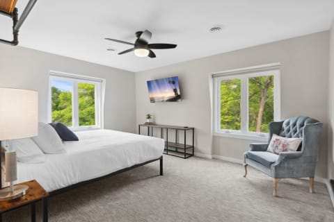Modern bedroom with a large window, stylish armchair, and mounted television.