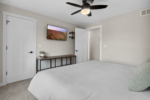 Modern bedroom with a bed, minimalist bench, and mounted television displaying a landscape photo.