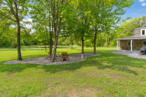 Outdoor seating area with wooden chairs under trees in a grassy setting.
