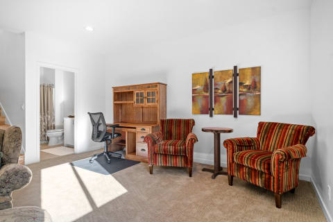A welcoming room featuring striped armchairs, a desk, and a bathroom doorway.