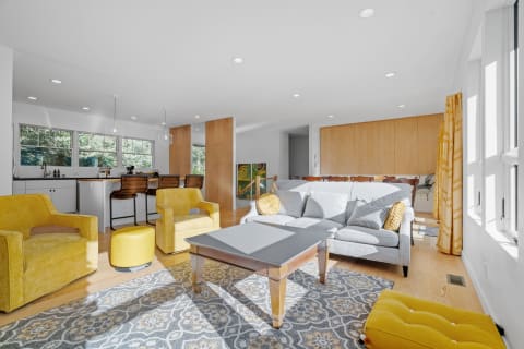 A modern living room with a grey sofa, yellow chairs, and a stylish kitchen in the background.