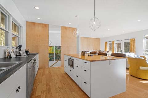 Modern kitchen featuring a wood countertop, white cabinets, and geometric pendant lights.