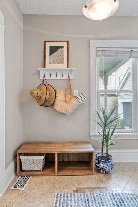 Cozy entryway with wood bench, straw hats, and a beach photo on a wall.