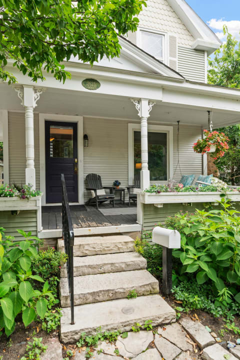 Front view of a charming house with a porch, steps, and lush plants.
