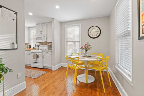 Bright kitchen space featuring a round table with yellow chairs and a flower arrangement.