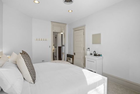 Bright serene bedroom with a large bed, white linens, and a small in-room sink.