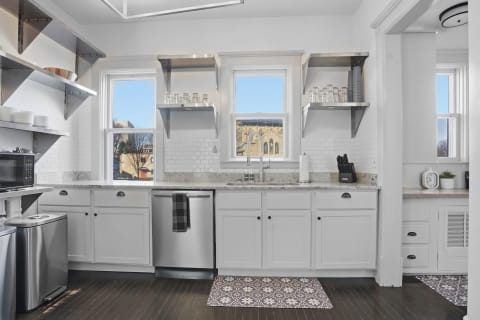 A bright kitchen with granite countertops, stainless steel appliances, and open shelves for dishware, framed by a city view outside the window.