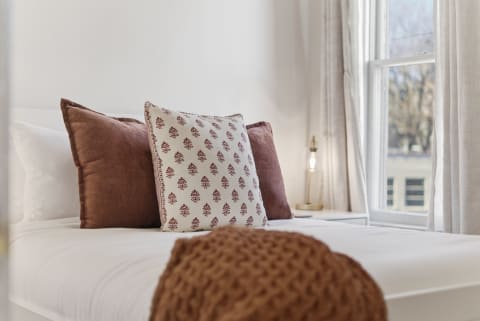 A close-up view of a cozy bed with plush pillows and soft linens, illuminated by natural light.