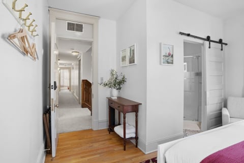 A well-decorated bedroom corner with a wooden floor, console table, and barn-style door to the bathroom.