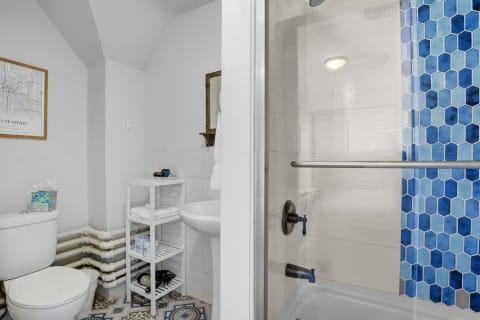 A modern bathroom featuring a white toilet, patterned floor tiles, and a shower with blue hexagon tiles.