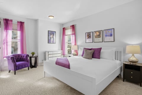 A modern bedroom featuring white bedding, a purple armchair, and vibrant decorations.