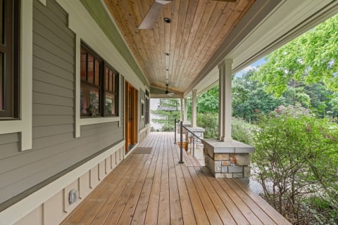 Porch area of a home featuring wooden decking and grey siding in a natural setting.