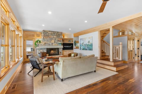 Modern living room with stone fireplace and wooden details, featuring a beige sofa and a staircase.