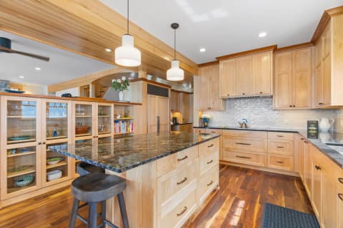Modern kitchen with wood cabinetry, granite island, and warm lighting.