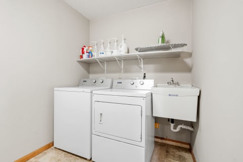 Laundry room with a washer, dryer, cleaning supplies, and a utility sink.