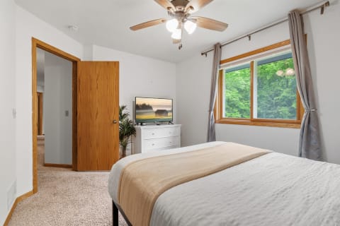 Cozy bedroom featuring a bed, dresser, and a large window with greenery outside.