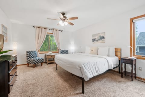 Modern bedroom with a double bed, accent chairs, and a lush green view through the window.