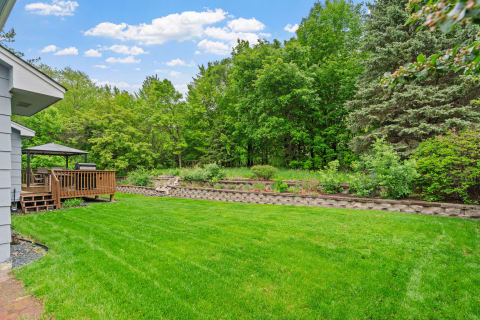 Backyard featuring a wooden deck, gazebo, and landscaped garden wall with greenery under a blue sky.