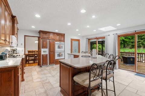 Modern kitchen with wooden cabinetry, large island, and outdoor deck visible through sliding doors.