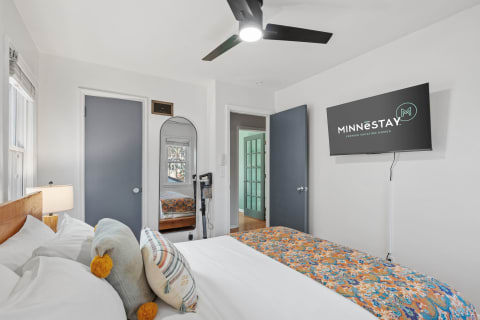 A stylish bedroom featuring a bed with colorful bedding, a flat-screen TV, and a mirror.