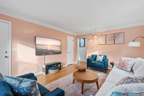 Cozy living room with peach walls, a white sectional couch, teal armchairs, and a mounted TV.