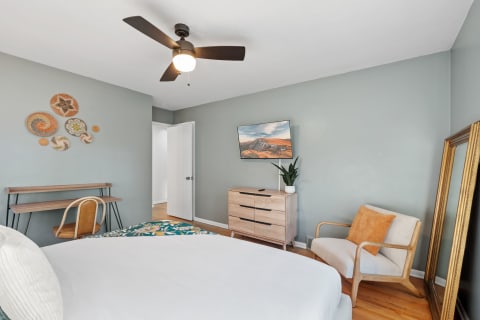 Cozy bedroom featuring decorative wall art, a bed, dresser, and a small desk area.