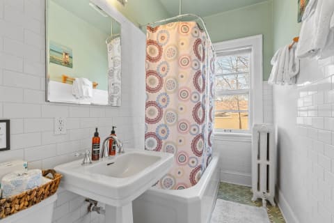 A vibrant bathroom with a patterned shower curtain, pedestal sink, and vintage elements.